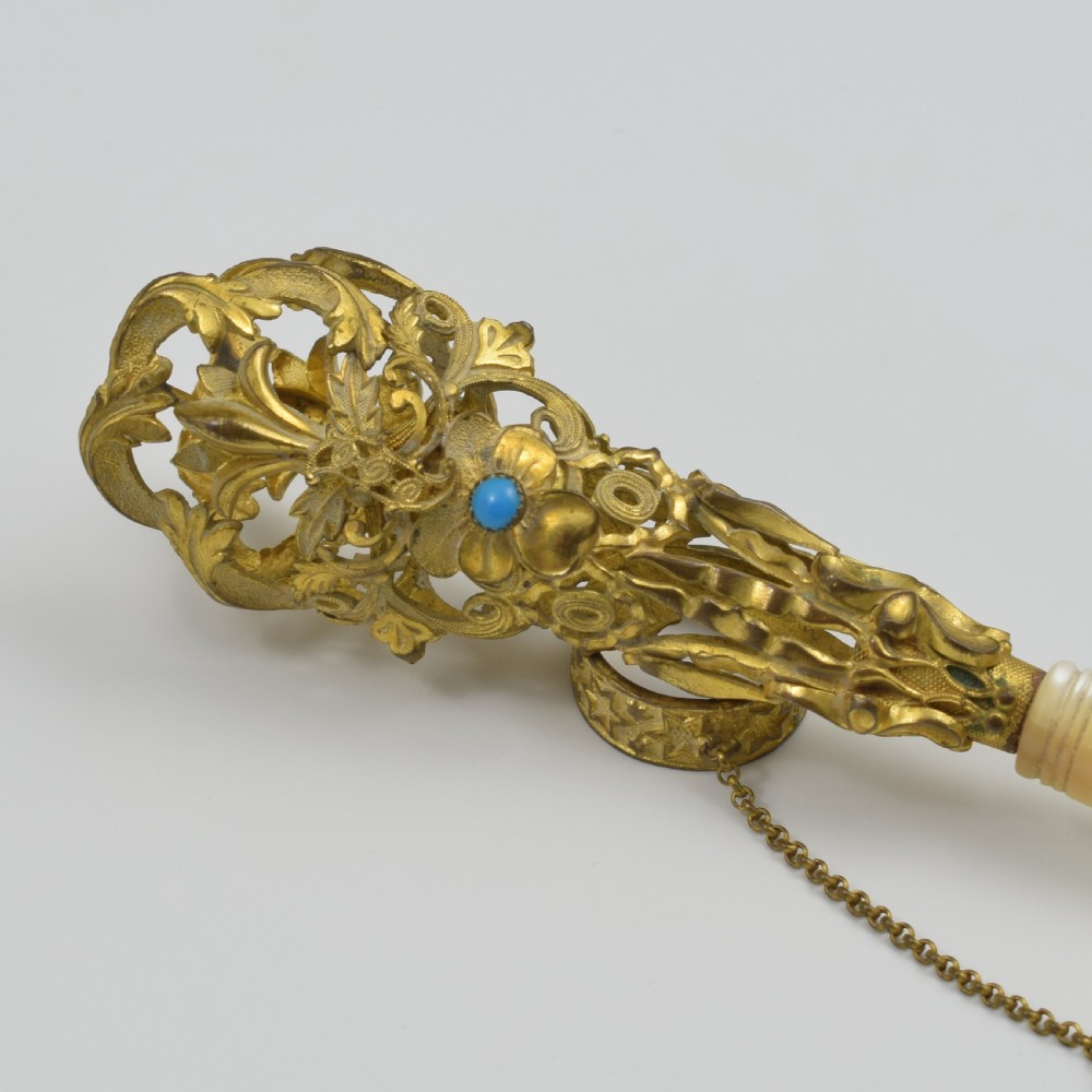 An antique French gilt ormolu tussie mussie posy holder featuring elaborate pierced metalwork set with a turquoise stone, a carved mother-of-pearl handle, and a finger ring attached by a chain. View VIII