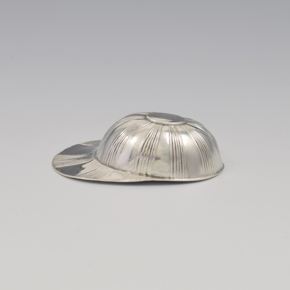 An antique Georgian sterling silver caddy spoon crafted in the realistic shape of a ribbed jockey cap. View IX