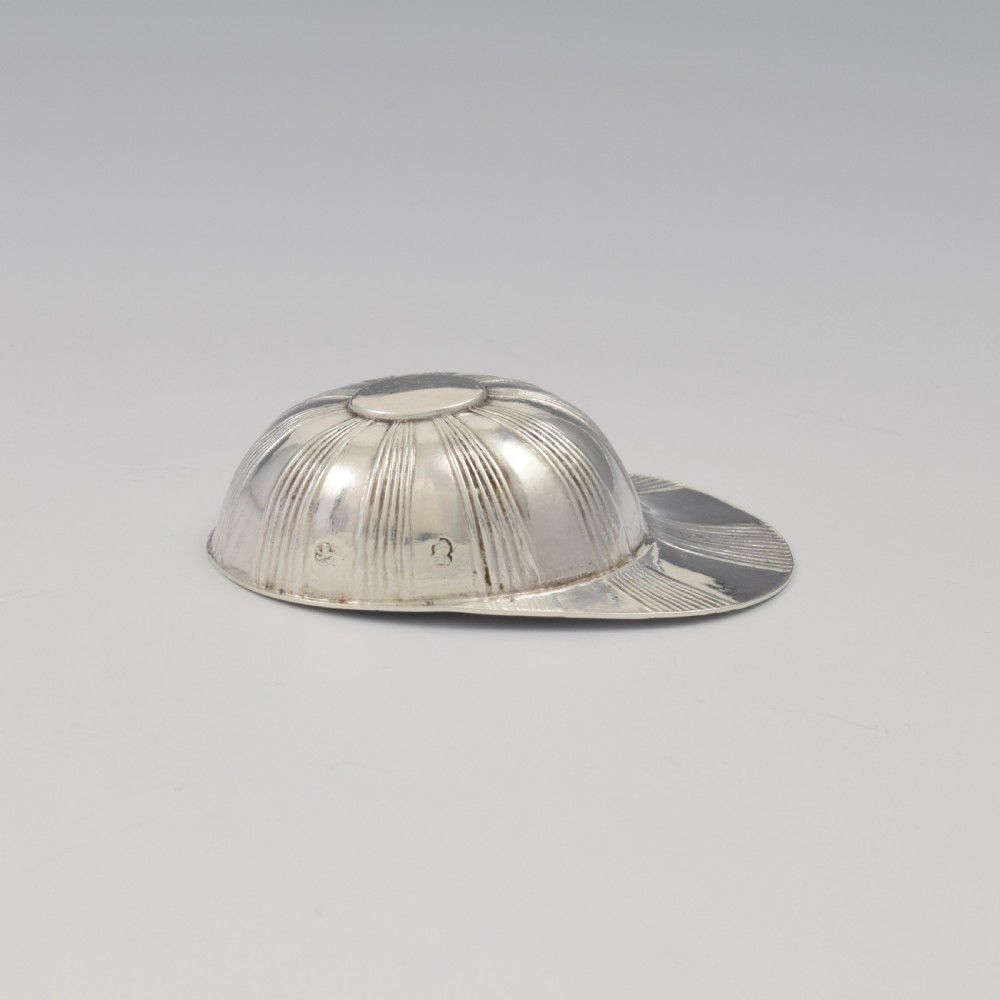 An antique Georgian sterling silver caddy spoon crafted in the realistic shape of a ribbed jockey cap. View XII