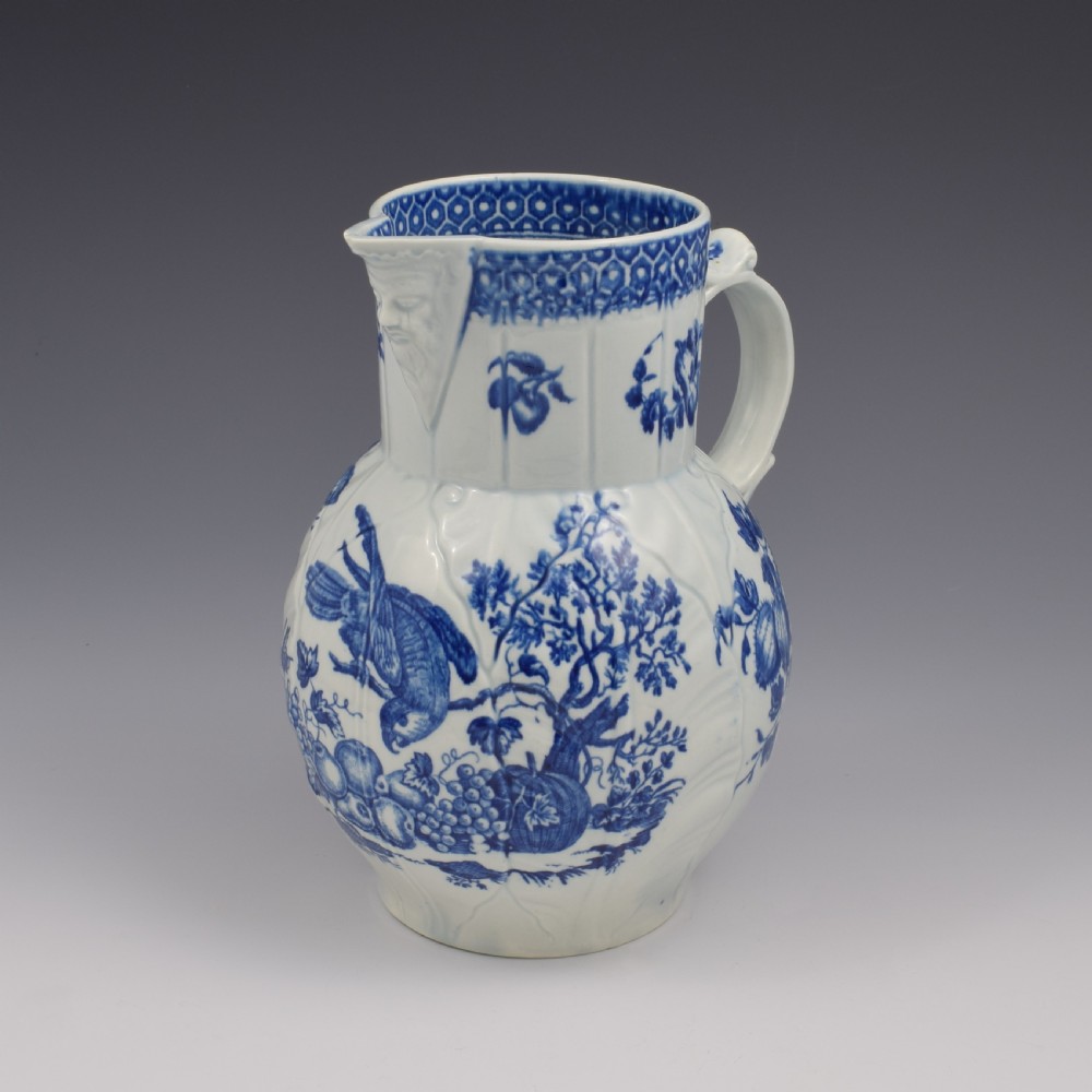 An 18th-century First Period Worcester soft-paste porcelain mask jug featuring cabbage-leaf moulding and blue and white printed foliage motifs.
