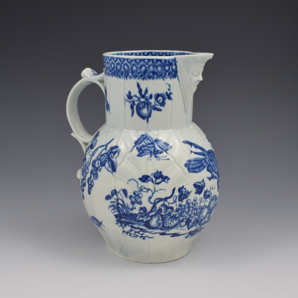 An 18th-century First Period Worcester soft-paste porcelain mask jug featuring cabbage-leaf moulding and blue and white printed foliage motifs. View V