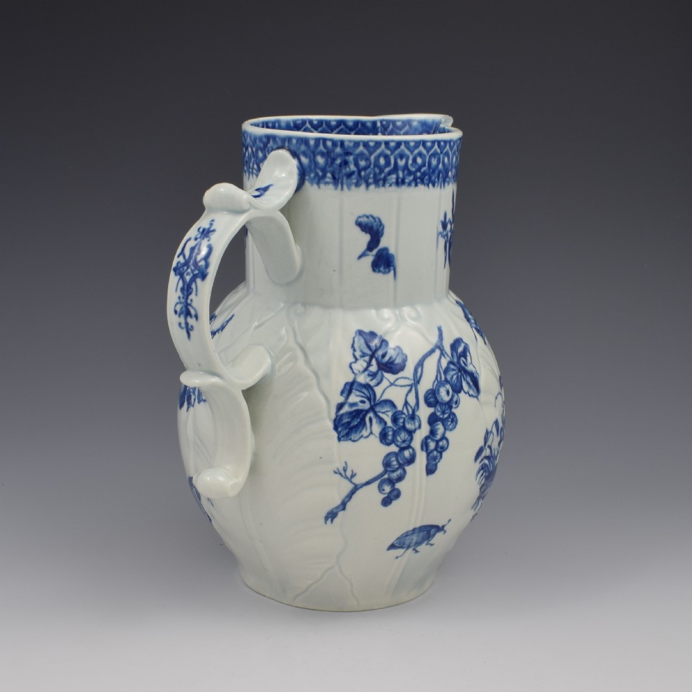 An 18th-century First Period Worcester soft-paste porcelain mask jug featuring cabbage-leaf moulding and blue and white printed foliage motifs. View VI