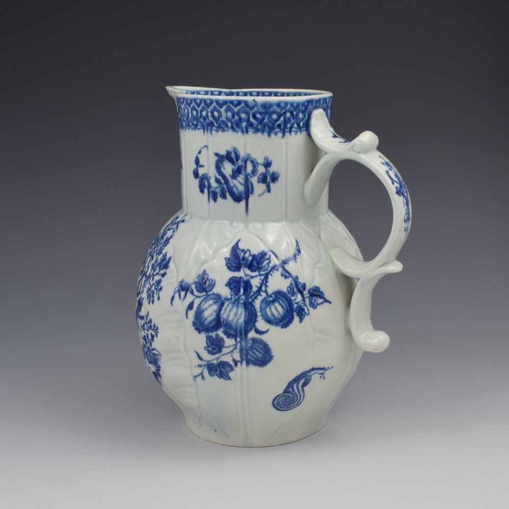 An 18th-century First Period Worcester soft-paste porcelain mask jug featuring cabbage-leaf moulding and blue and white printed foliage motifs. View X