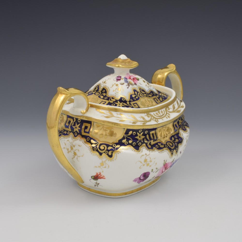 A Regency period lidded porcelain sucrier featuring twin handles, cobalt blue borders decorated with gilt Greek key scrolling, and hand-painted floral sprays. View III