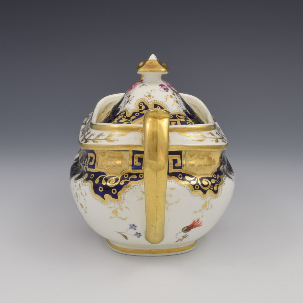 A Regency period lidded porcelain sucrier featuring twin handles, cobalt blue borders decorated with gilt Greek key scrolling, and hand-painted floral sprays. View IV