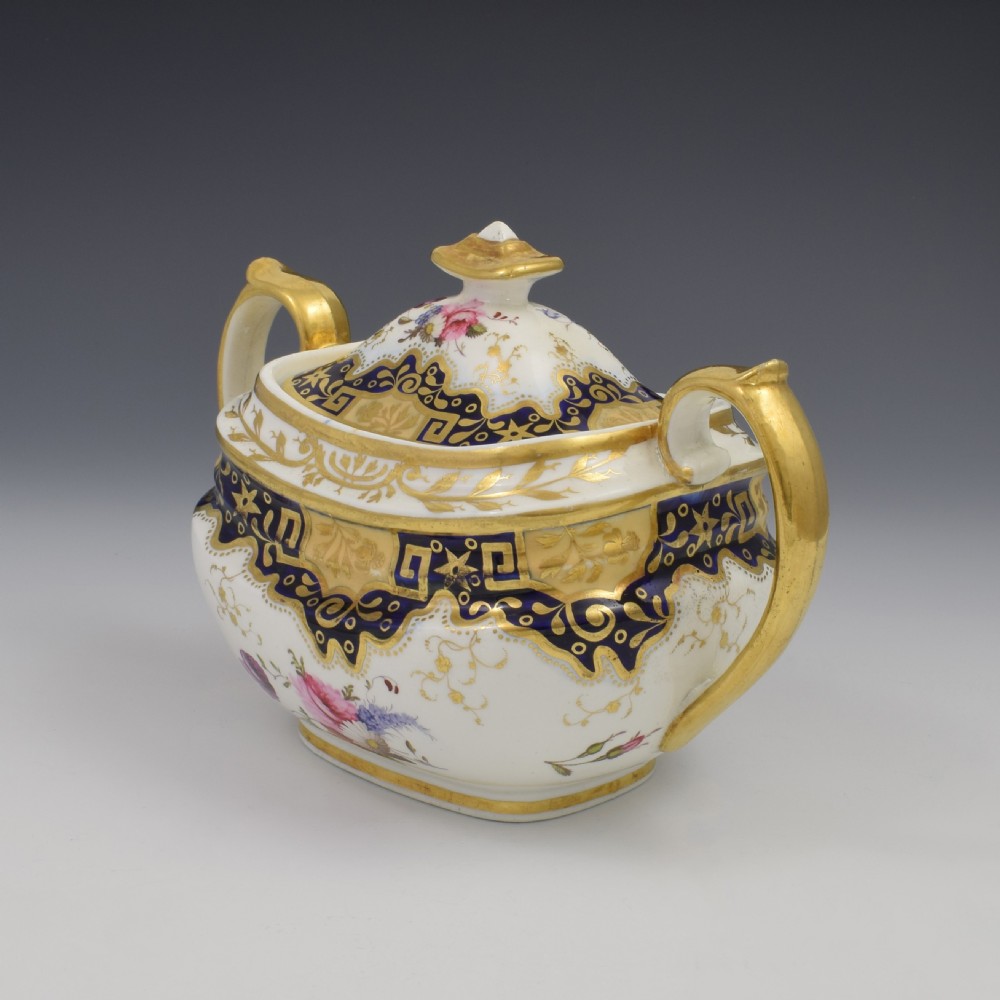 A Regency period lidded porcelain sucrier featuring twin handles, cobalt blue borders decorated with gilt Greek key scrolling, and hand-painted floral sprays. View XI