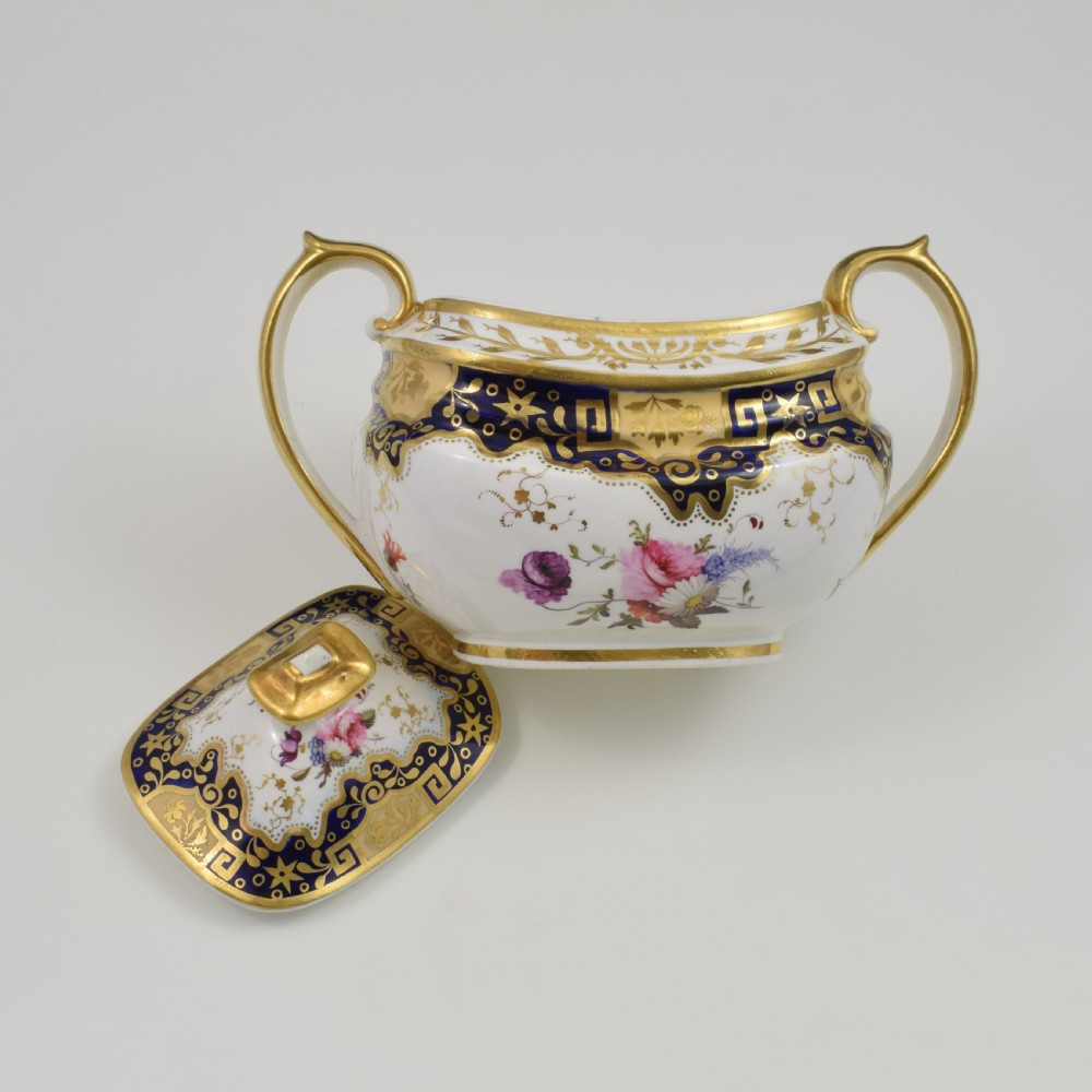 A Regency period lidded porcelain sucrier featuring twin handles, cobalt blue borders decorated with gilt Greek key scrolling, and hand-painted floral sprays. View XIII