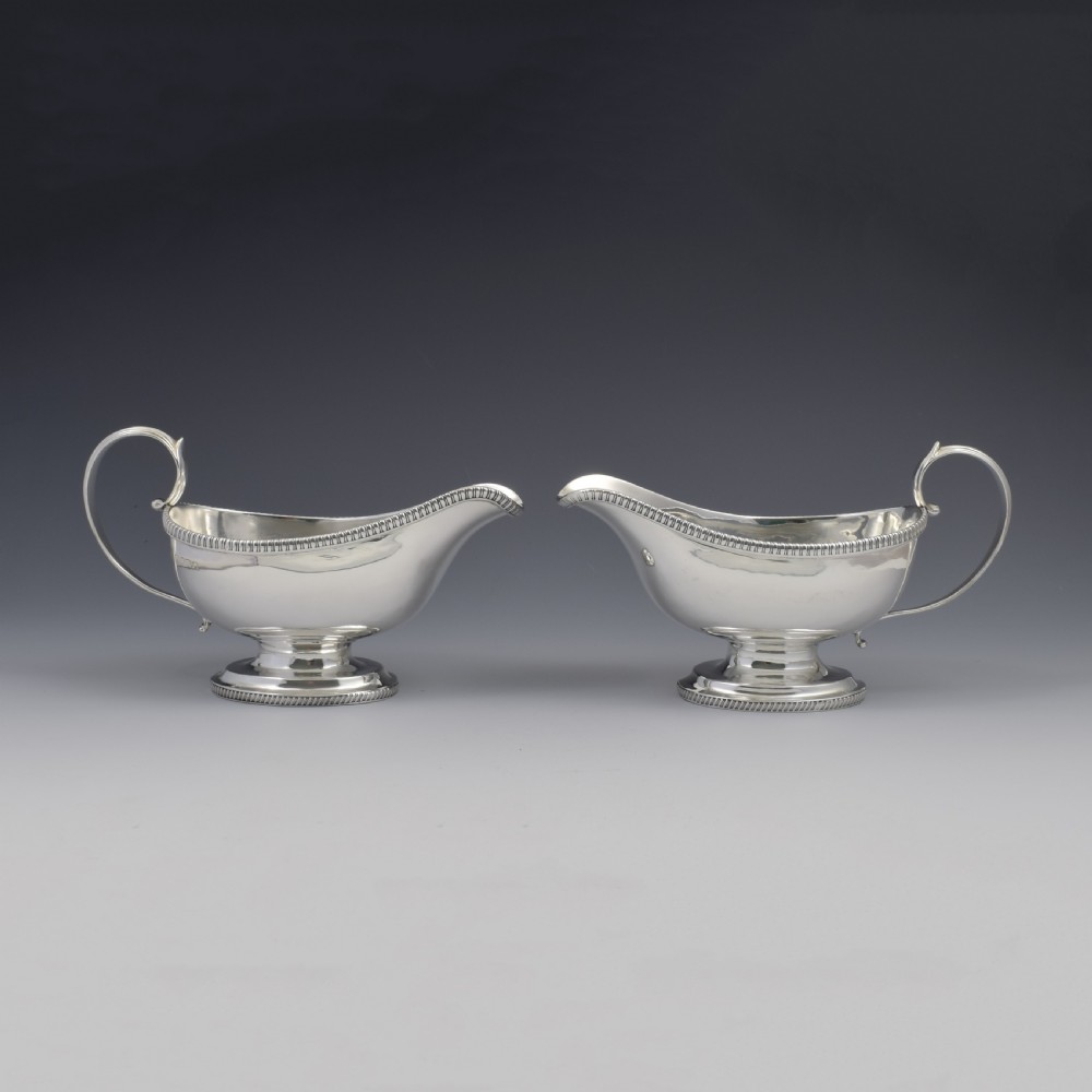 A pair of polished Georgian sterling silver sauce boats featuring gadrooned rims, flying scroll handles, and flared pedestal bases.
