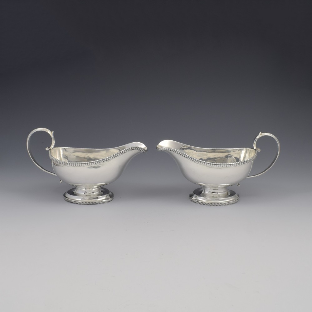 A pair of polished Georgian sterling silver sauce boats featuring gadrooned rims, flying scroll handles, and flared pedestal bases. View II