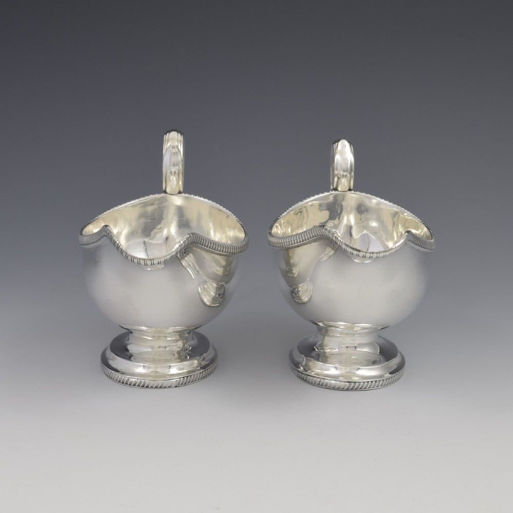 A pair of polished Georgian sterling silver sauce boats featuring gadrooned rims, flying scroll handles, and flared pedestal bases. View III