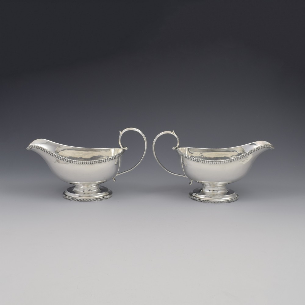 A pair of polished Georgian sterling silver sauce boats featuring gadrooned rims, flying scroll handles, and flared pedestal bases. View V