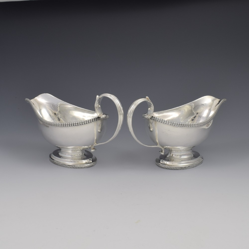 A pair of polished Georgian sterling silver sauce boats featuring gadrooned rims, flying scroll handles, and flared pedestal bases. View VI