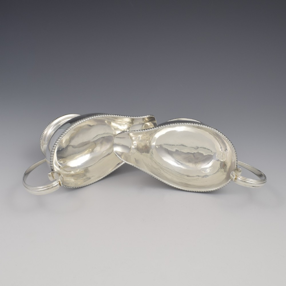 A pair of polished Georgian sterling silver sauce boats featuring gadrooned rims, flying scroll handles, and flared pedestal bases. View VII