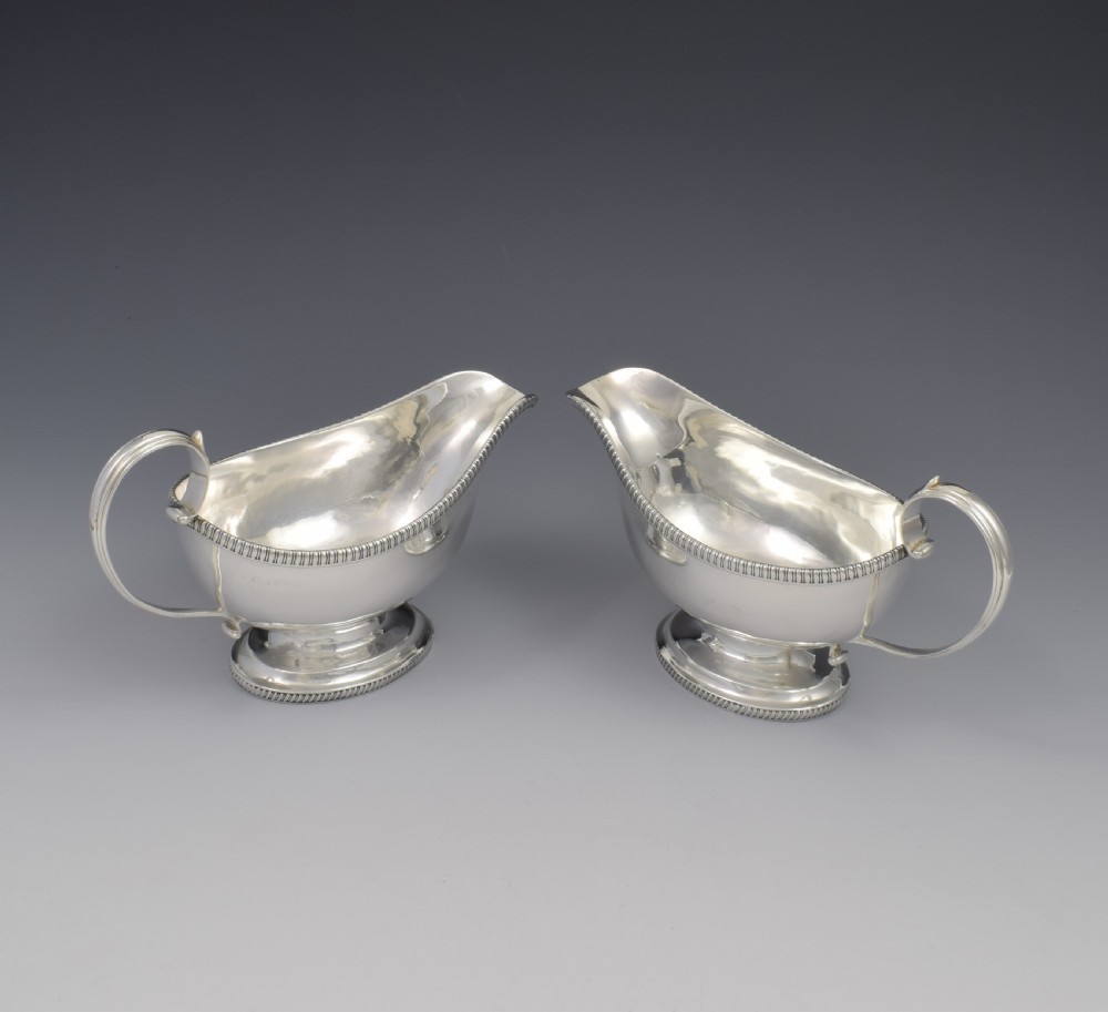 A pair of polished Georgian sterling silver sauce boats featuring gadrooned rims, flying scroll handles, and flared pedestal bases. View IX