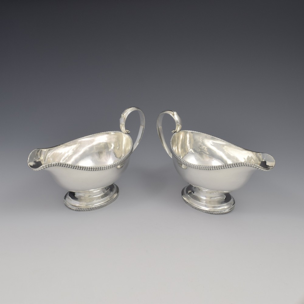 A pair of polished Georgian sterling silver sauce boats featuring gadrooned rims, flying scroll handles, and flared pedestal bases. View XVI