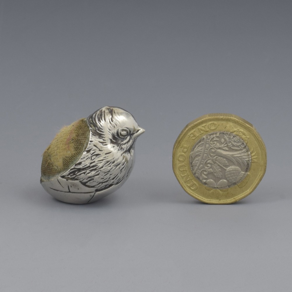 An Edwardian sterling silver pin cushion in the shape of a hatching chick emerging from an egg shell with a fabric insert on its back.