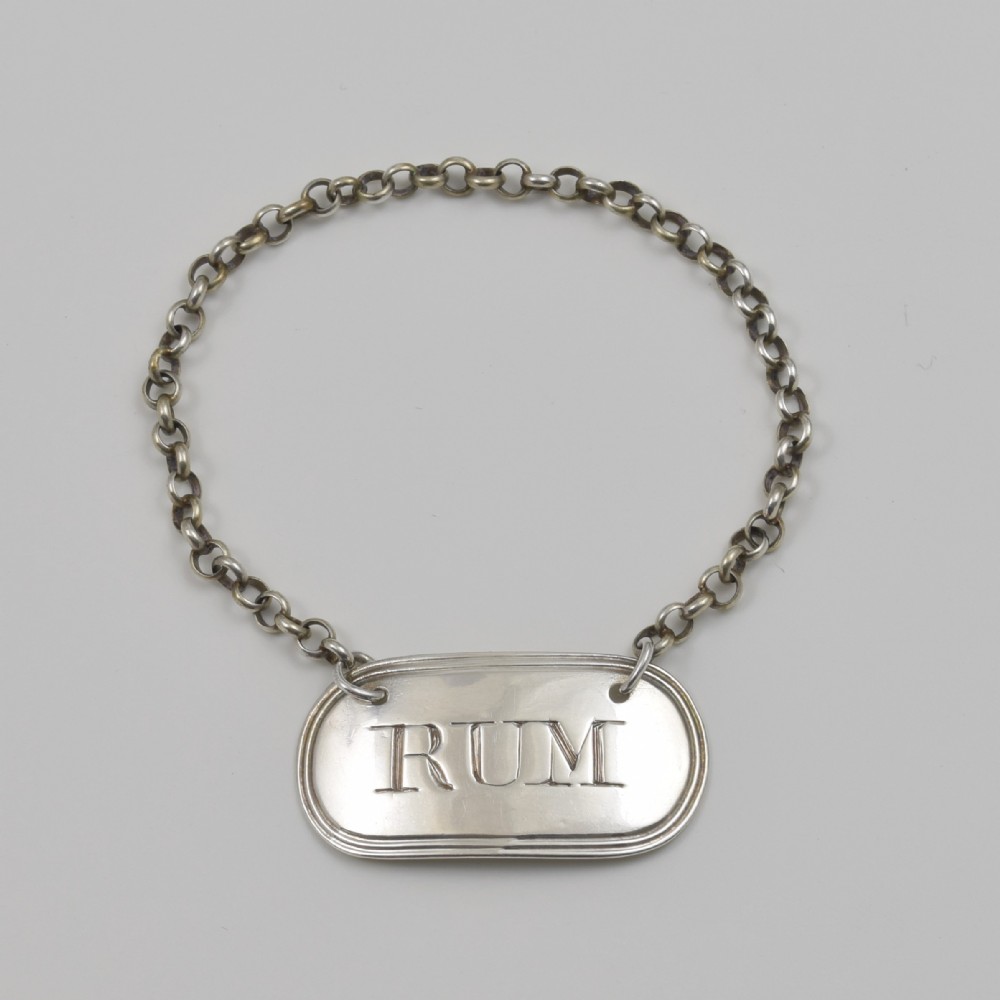 An oblong Georgian sterling silver decanter label engraved with RUM and suspended from a silver chain.