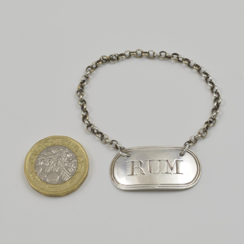 An oblong Georgian sterling silver decanter label engraved with RUM and suspended from a silver chain. View III