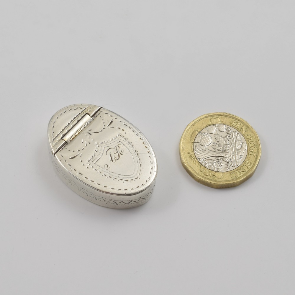 An oval Georgian sterling silver box featuring bright-cut engraved border patterns, foliage details, and a central shield motif with initials. View III
