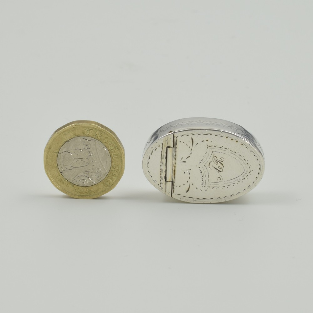 An oval Georgian sterling silver box featuring bright-cut engraved border patterns, foliage details, and a central shield motif with initials. View VIII
