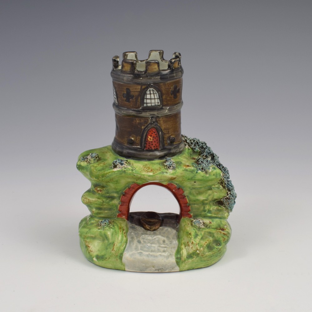 An antique Staffordshire pearlware spill vase shaped as a brown castellated turret standing over a green rocky bridge with a small boat underneath. View II