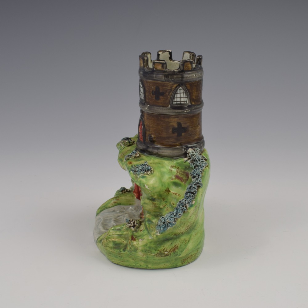 An antique Staffordshire pearlware spill vase shaped as a brown castellated turret standing over a green rocky bridge with a small boat underneath. View V