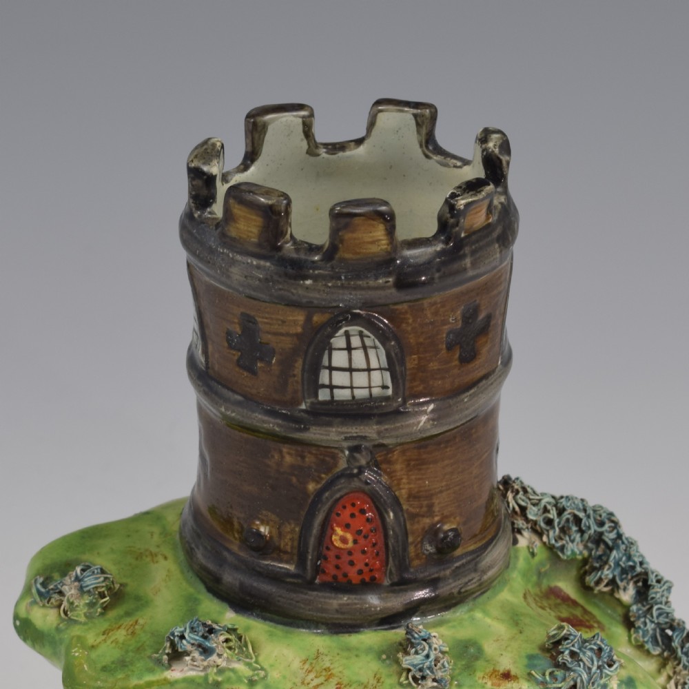 An antique Staffordshire pearlware spill vase shaped as a brown castellated turret standing over a green rocky bridge with a small boat underneath. View IX