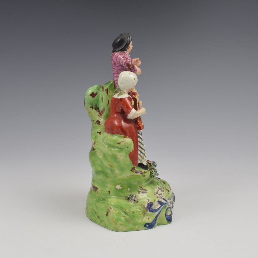 An antique Staffordshire pearlware figure group titled Songsters depicting a seated woman playing an instrument alongside a standing man, a dog, and a swan on a green mound base. View III