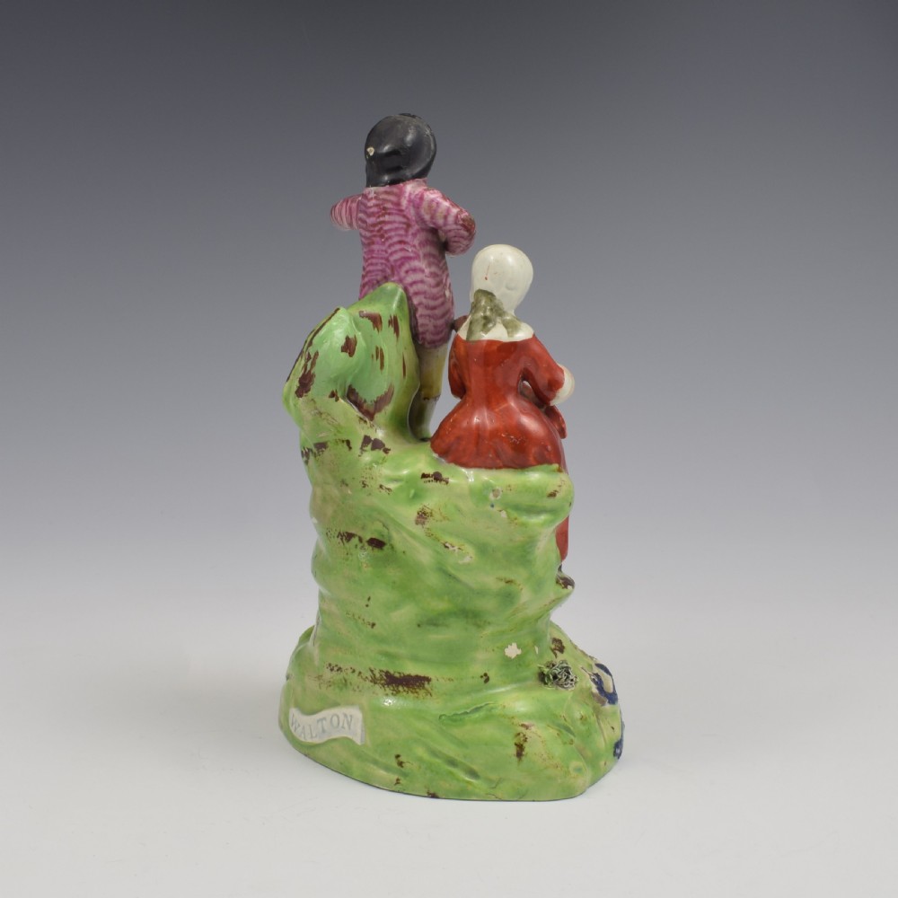 An antique Staffordshire pearlware figure group titled Songsters depicting a seated woman playing an instrument alongside a standing man, a dog, and a swan on a green mound base. View IV