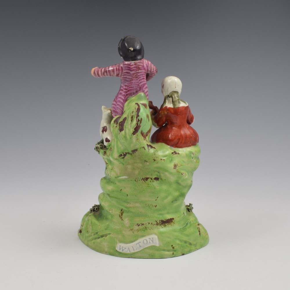 An antique Staffordshire pearlware figure group titled Songsters depicting a seated woman playing an instrument alongside a standing man, a dog, and a swan on a green mound base. View V