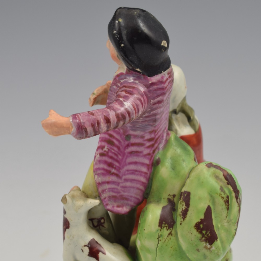 An antique Staffordshire pearlware figure group titled Songsters depicting a seated woman playing an instrument alongside a standing man, a dog, and a swan on a green mound base. View X