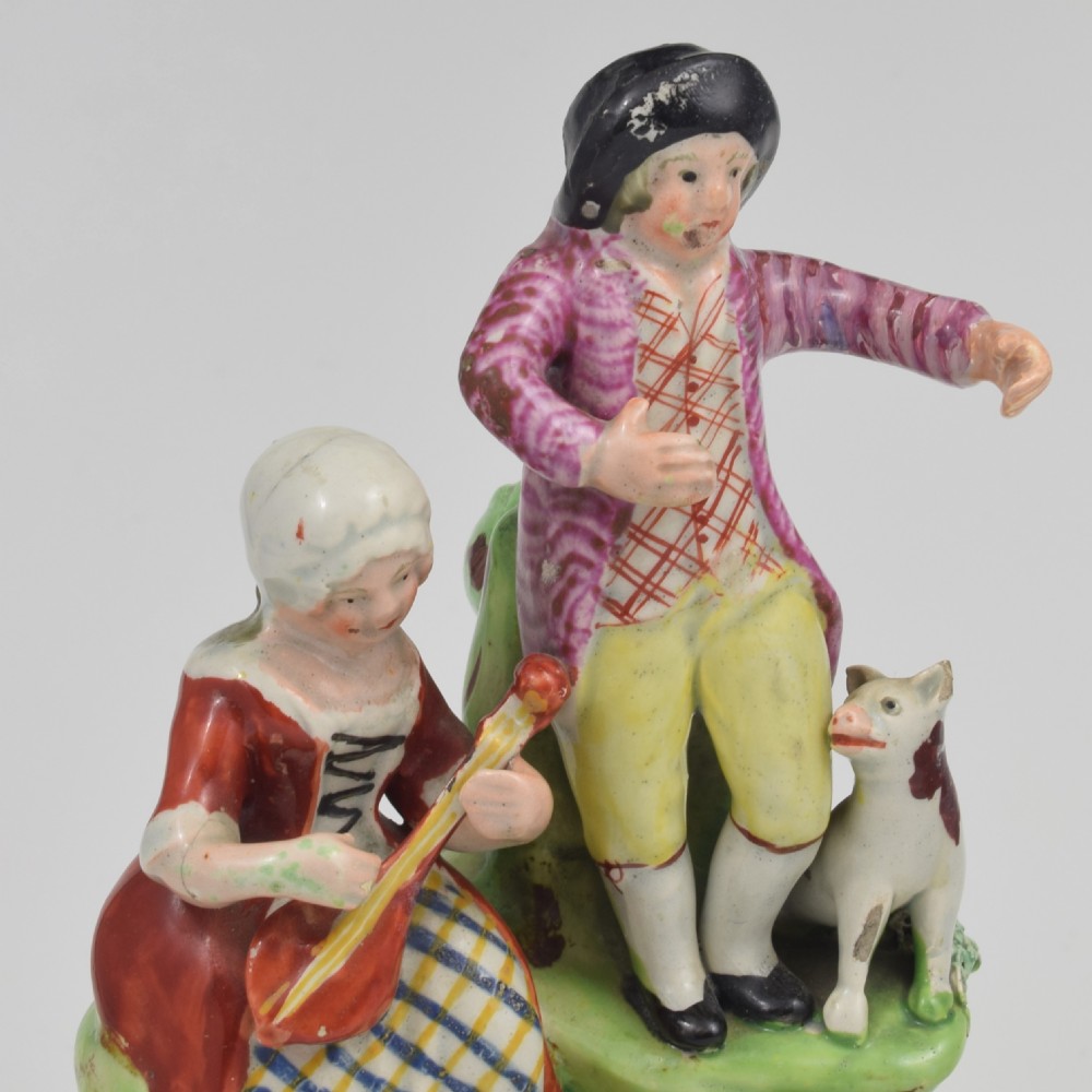 An antique Staffordshire pearlware figure group titled Songsters depicting a seated woman playing an instrument alongside a standing man, a dog, and a swan on a green mound base. View XIII