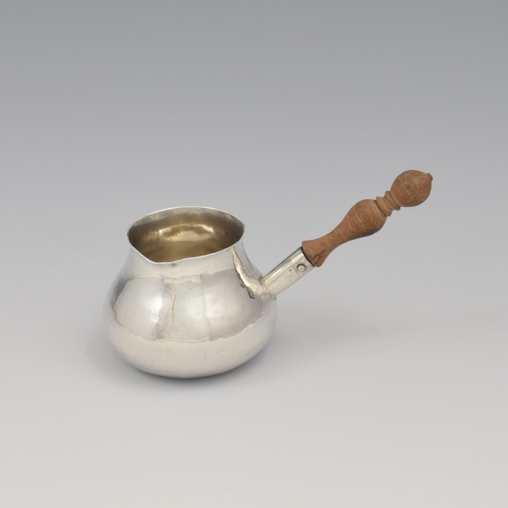A miniature George I sterling silver brandy warming pan featuring a bulbous body, small spout, and a turned wooden handle.
