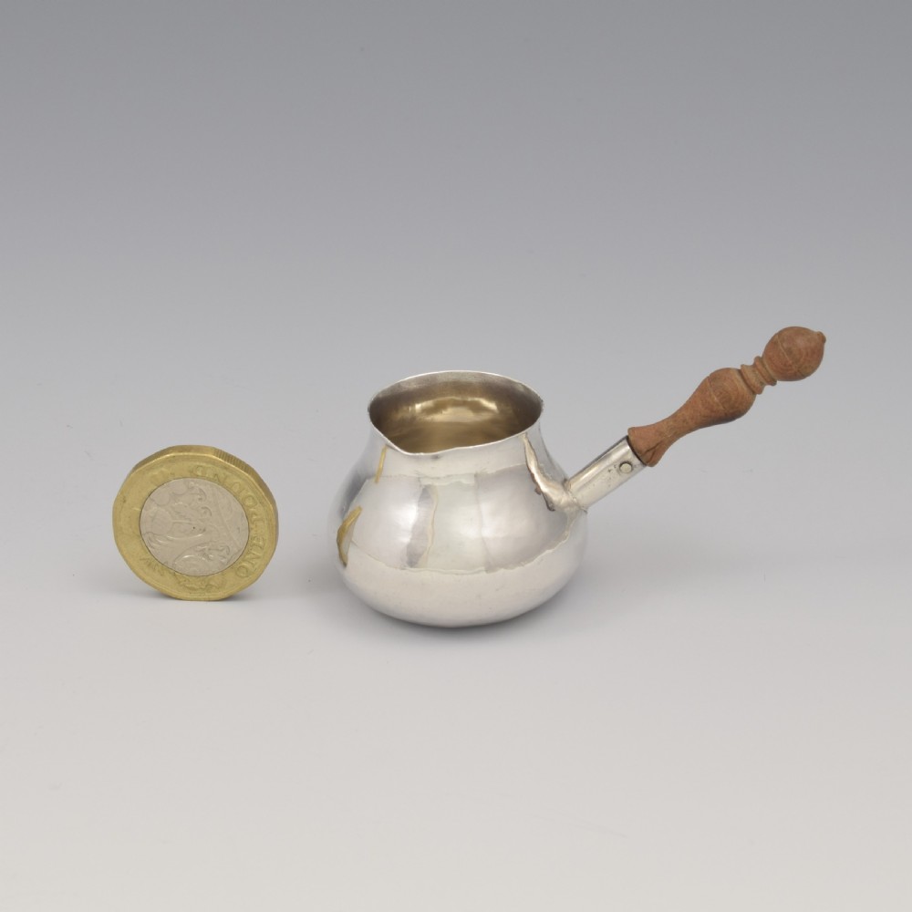 A miniature George I sterling silver brandy warming pan featuring a bulbous body, small spout, and a turned wooden handle. View II
