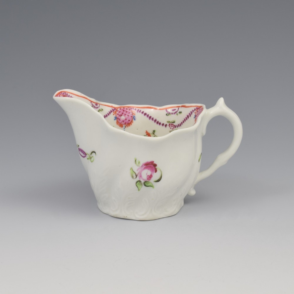 A white porcelain low Chelsea ewer cream jug featuring hand-painted pink floral sprigs, a moulded leaf base, and an ornate loop handle.