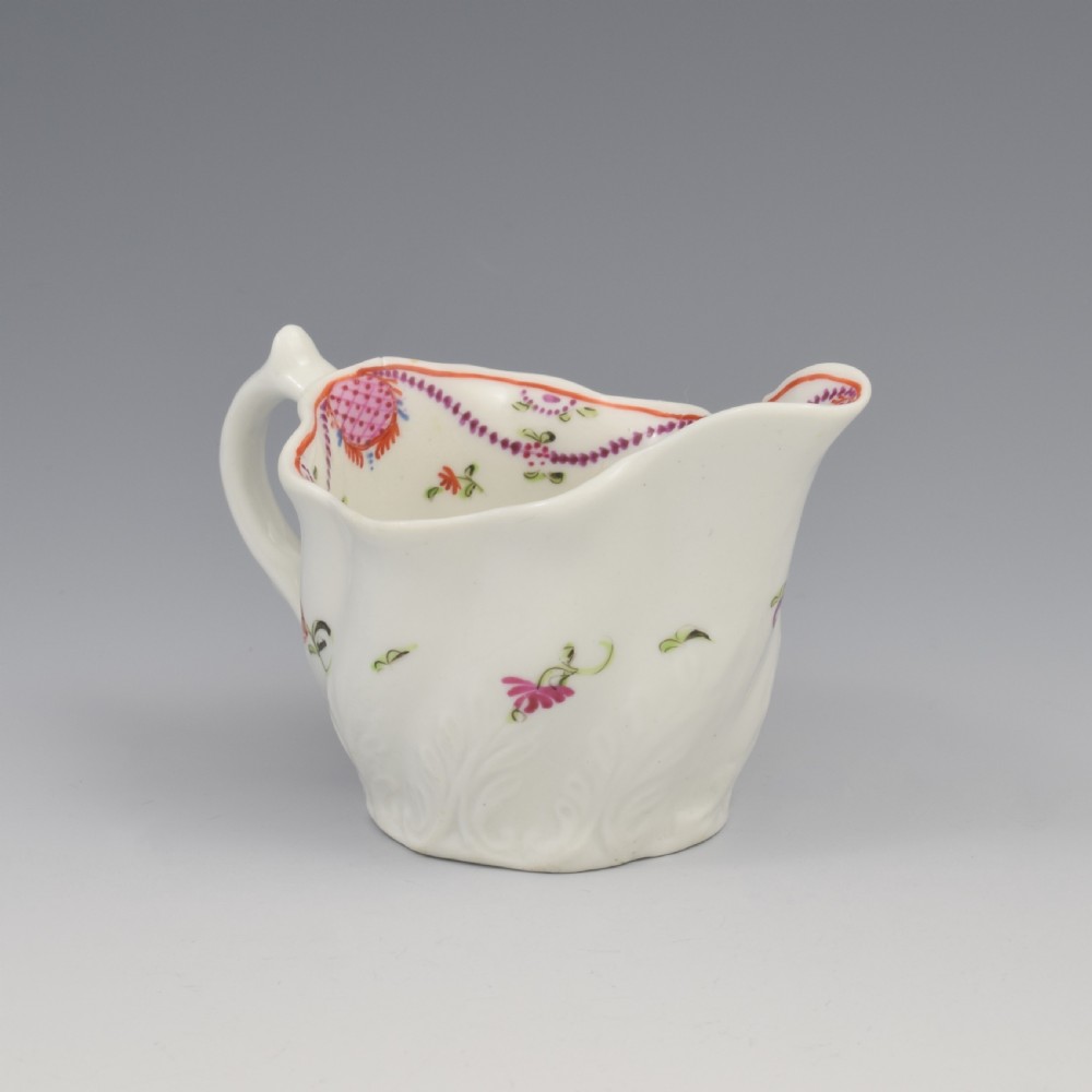 A white porcelain low Chelsea ewer cream jug featuring hand-painted pink floral sprigs, a moulded leaf base, and an ornate loop handle. View IV