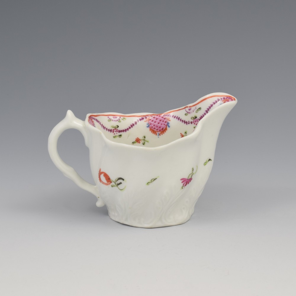 A white porcelain low Chelsea ewer cream jug featuring hand-painted pink floral sprigs, a moulded leaf base, and an ornate loop handle. View V