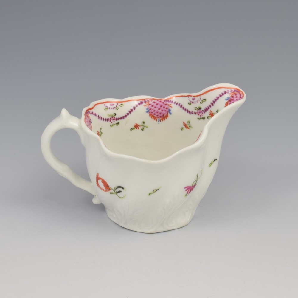 A white porcelain low Chelsea ewer cream jug featuring hand-painted pink floral sprigs, a moulded leaf base, and an ornate loop handle. View VI