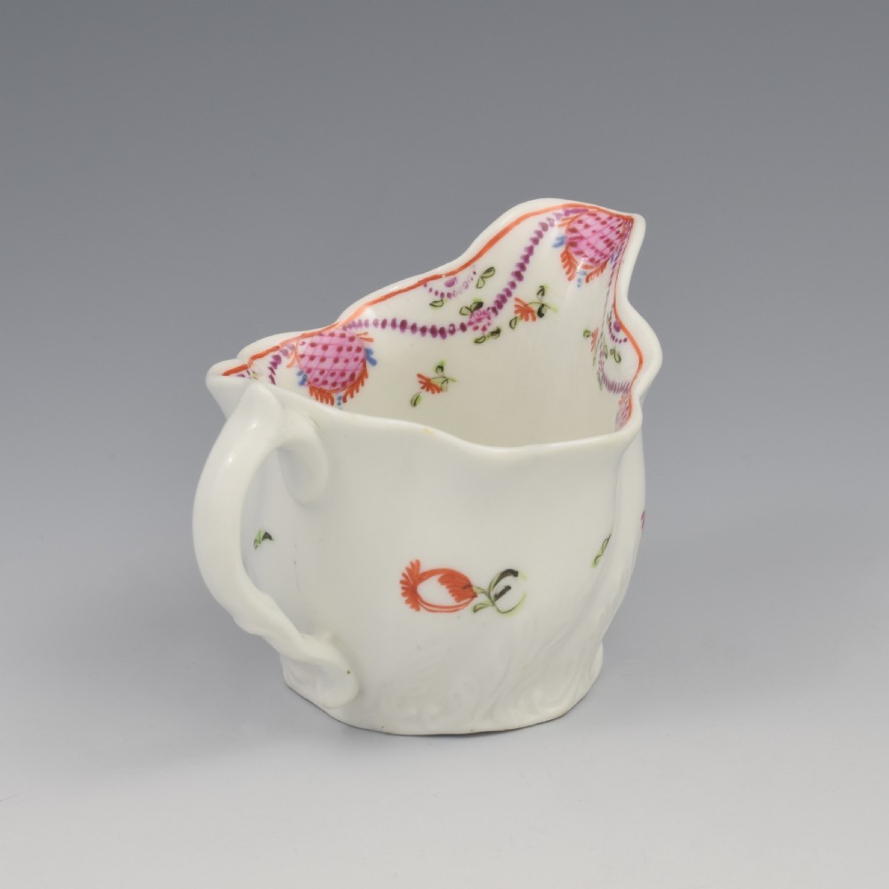 A white porcelain low Chelsea ewer cream jug featuring hand-painted pink floral sprigs, a moulded leaf base, and an ornate loop handle. View VII