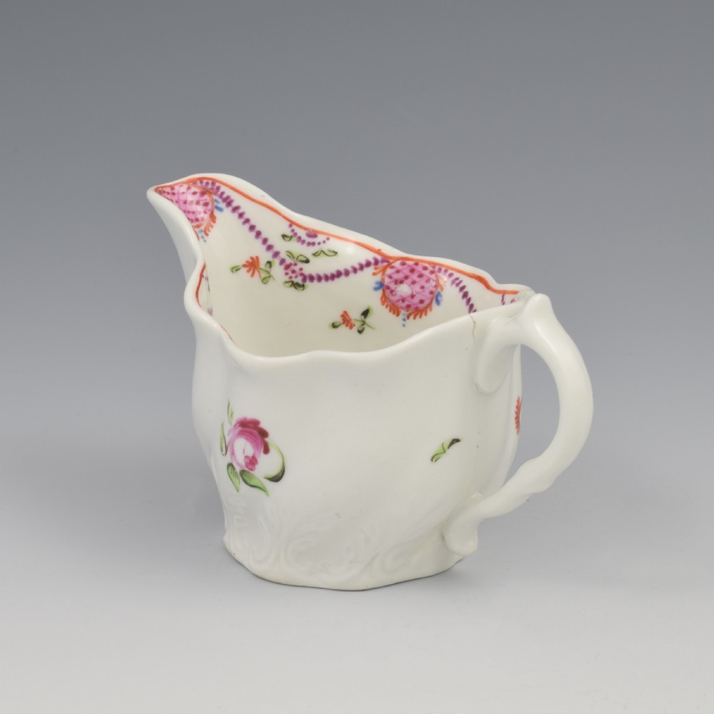 A white porcelain low Chelsea ewer cream jug featuring hand-painted pink floral sprigs, a moulded leaf base, and an ornate loop handle. View IX