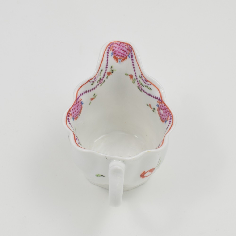 A white porcelain low Chelsea ewer cream jug featuring hand-painted pink floral sprigs, a moulded leaf base, and an ornate loop handle. View X