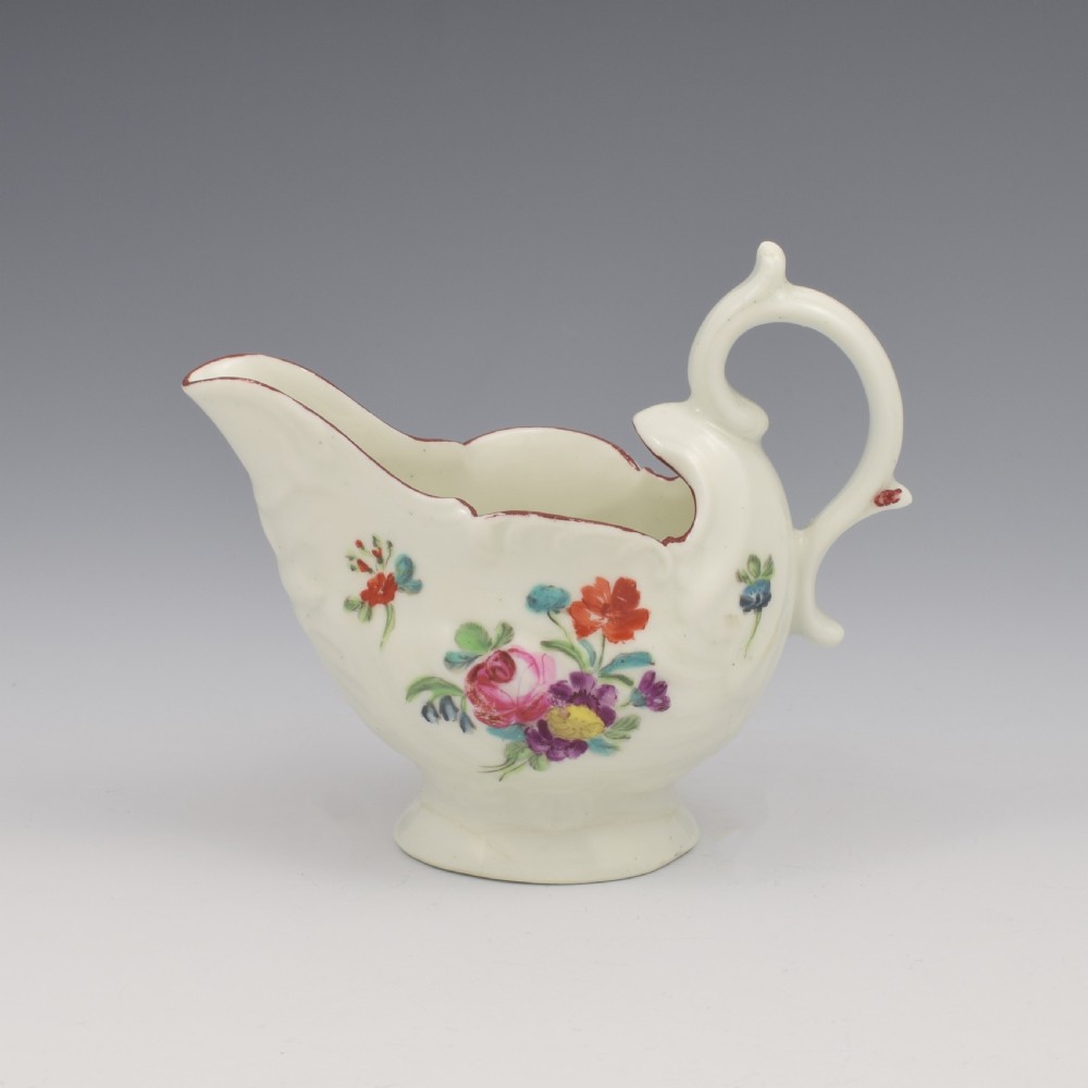 A Georgian Derby soft-paste porcelain cream boat with hand-painted floral motifs and a shaped loop handle on a pedestal base.