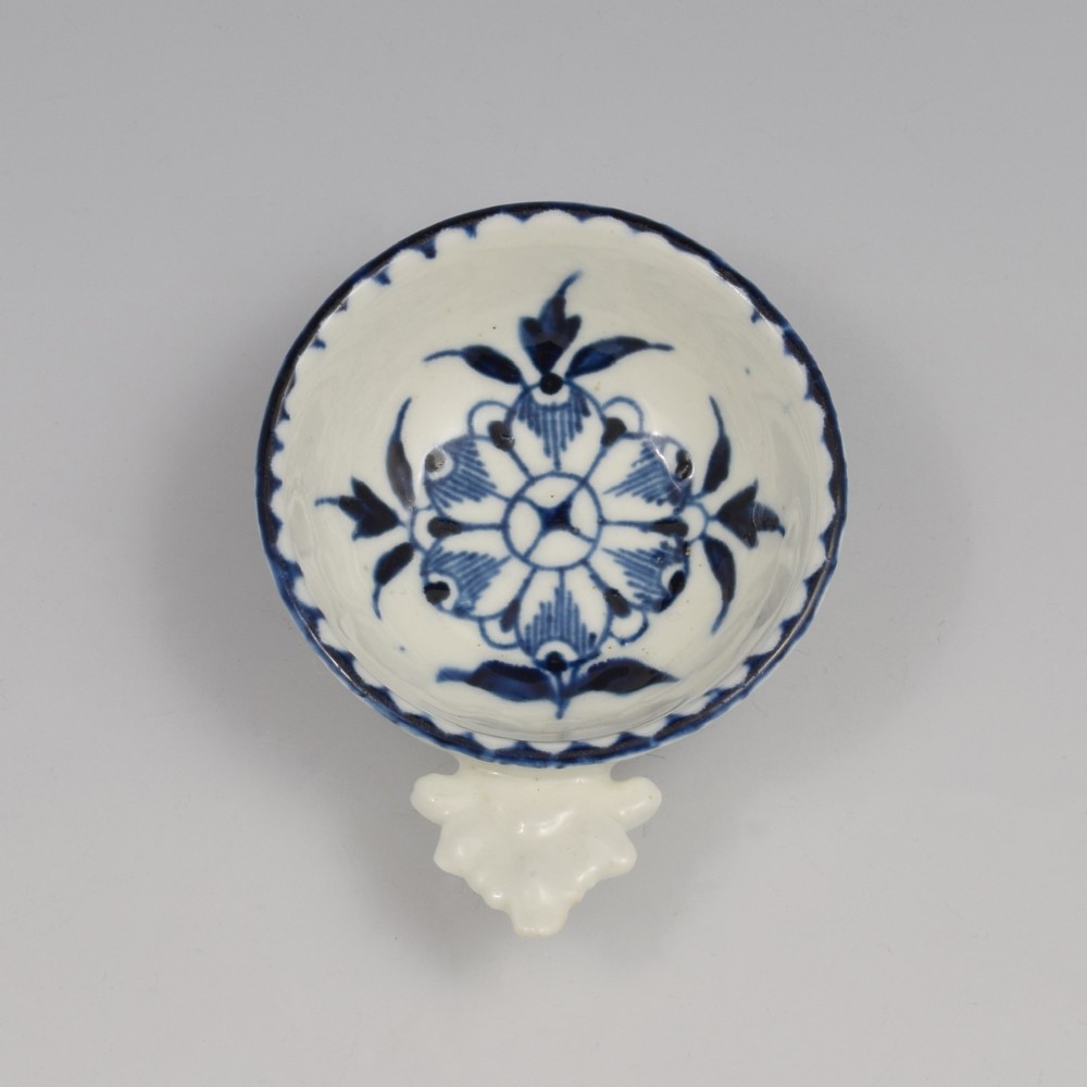 An eighteenth-century Derby soft-paste porcelain circular wine taster featuring hand-painted underglaze blue floral motifs and a shell-moulded handle.