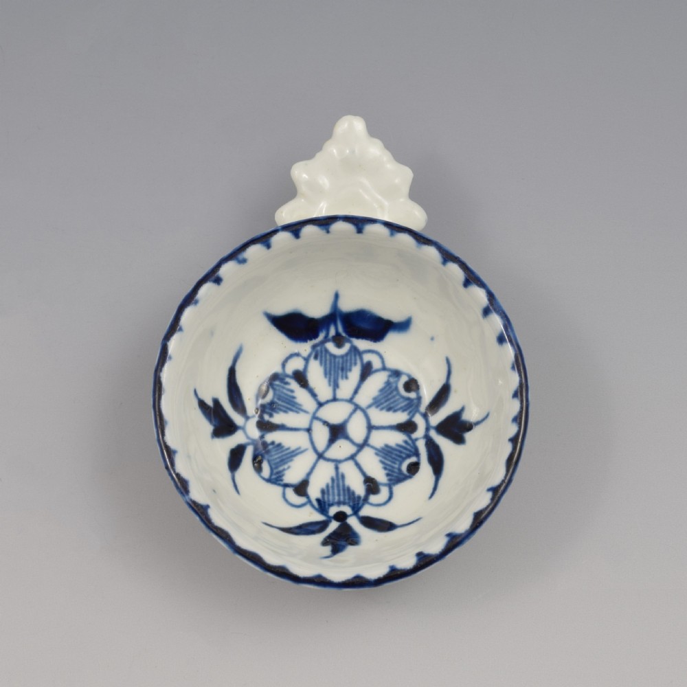An eighteenth-century Derby soft-paste porcelain circular wine taster featuring hand-painted underglaze blue floral motifs and a shell-moulded handle. View IV
