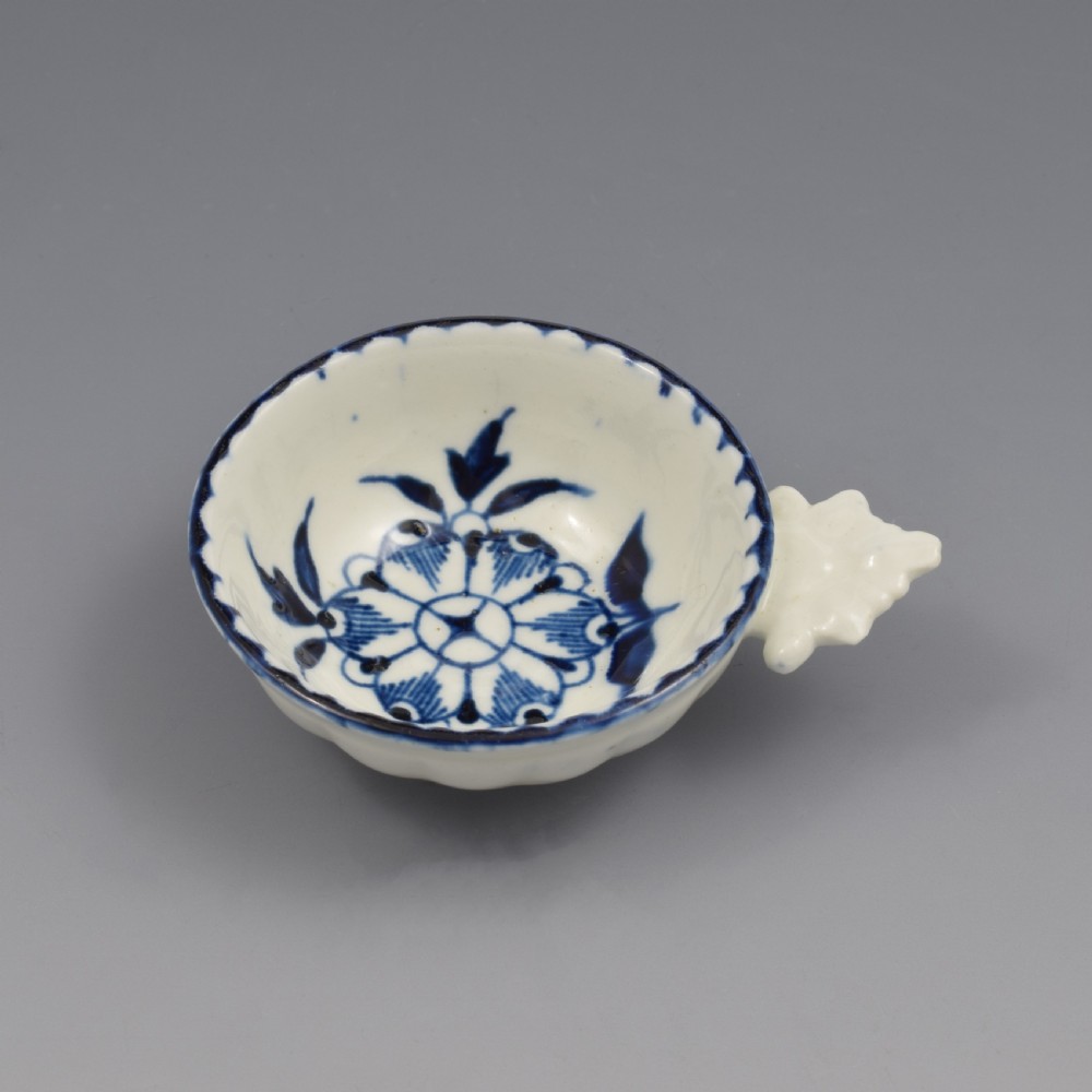 An eighteenth-century Derby soft-paste porcelain circular wine taster featuring hand-painted underglaze blue floral motifs and a shell-moulded handle. View V