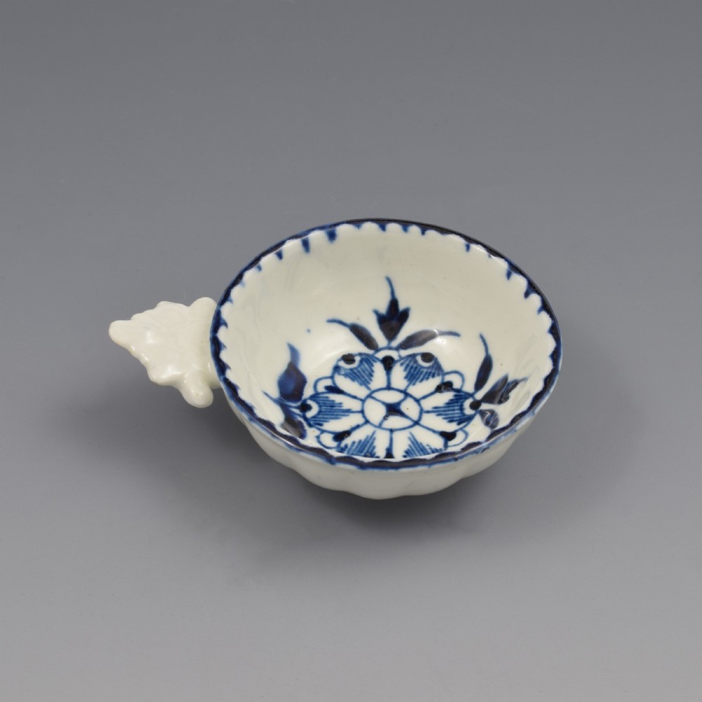 An eighteenth-century Derby soft-paste porcelain circular wine taster featuring hand-painted underglaze blue floral motifs and a shell-moulded handle. View VI