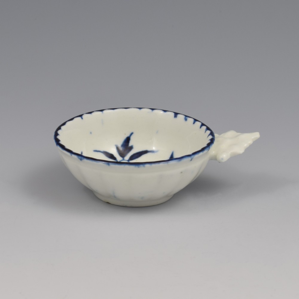 An eighteenth-century Derby soft-paste porcelain circular wine taster featuring hand-painted underglaze blue floral motifs and a shell-moulded handle. View IX