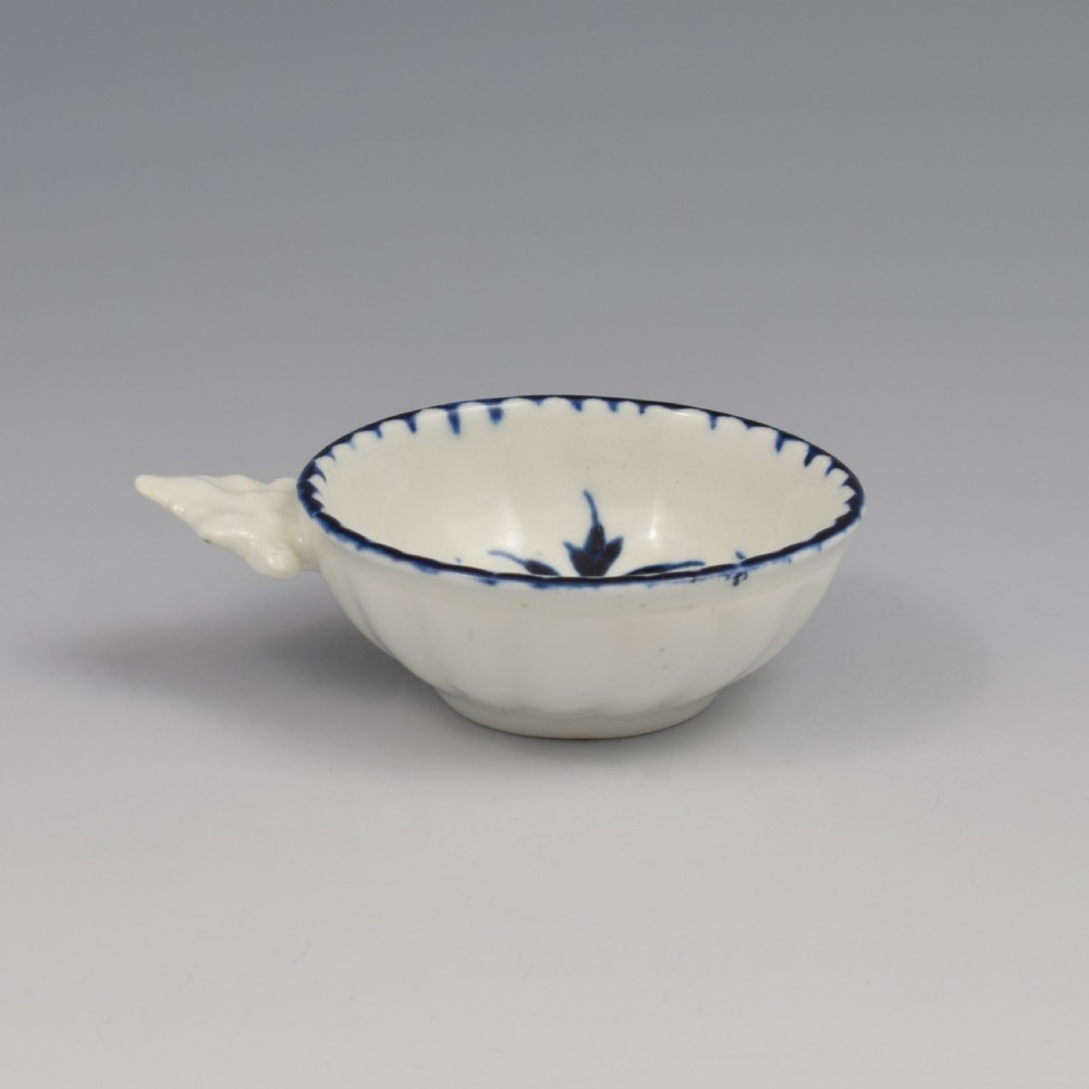 An eighteenth-century Derby soft-paste porcelain circular wine taster featuring hand-painted underglaze blue floral motifs and a shell-moulded handle. View X