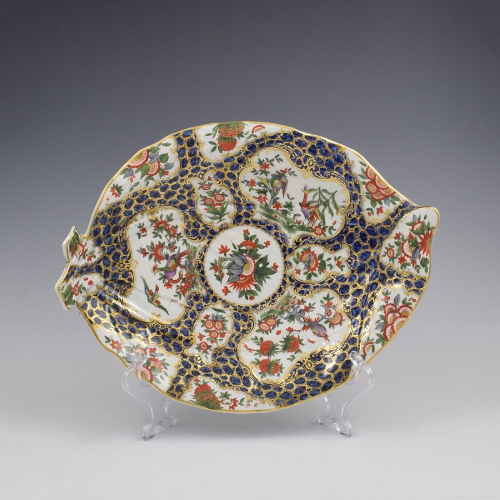 An eighteenth-century Worcester soft-paste porcelain leaf-shaped dish decorated with dark blue cailloute ground, gilded reserves, and hand-painted Kakiemon floral and bird motifs.