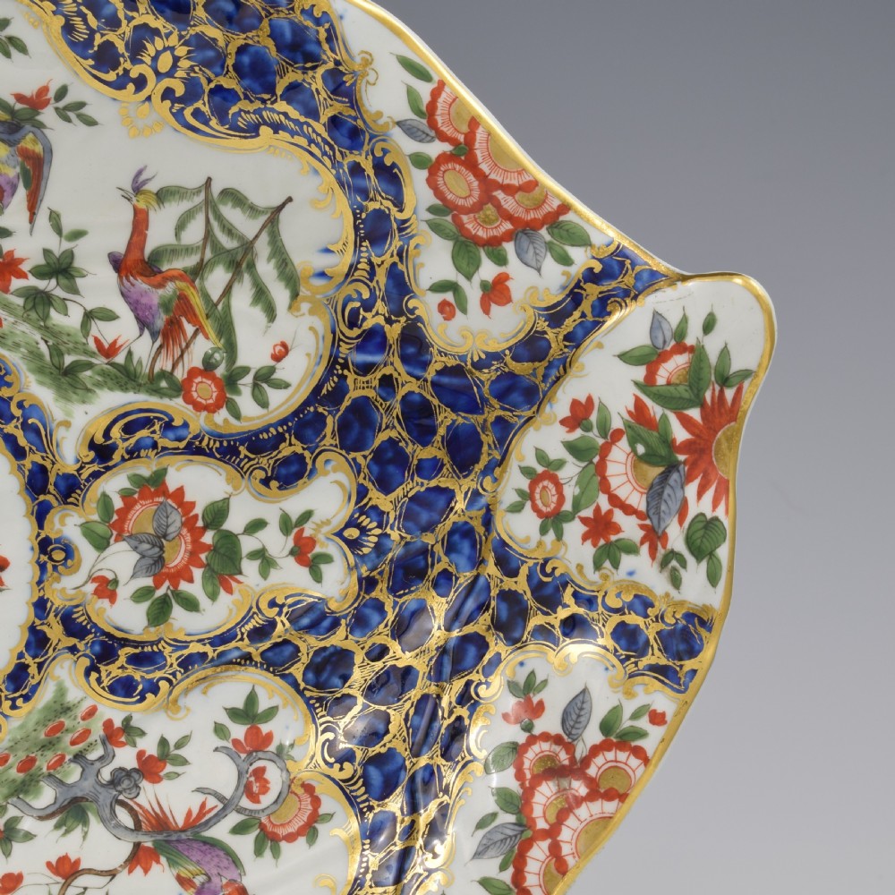 An eighteenth-century Worcester soft-paste porcelain leaf-shaped dish decorated with dark blue cailloute ground, gilded reserves, and hand-painted Kakiemon floral and bird motifs. View II